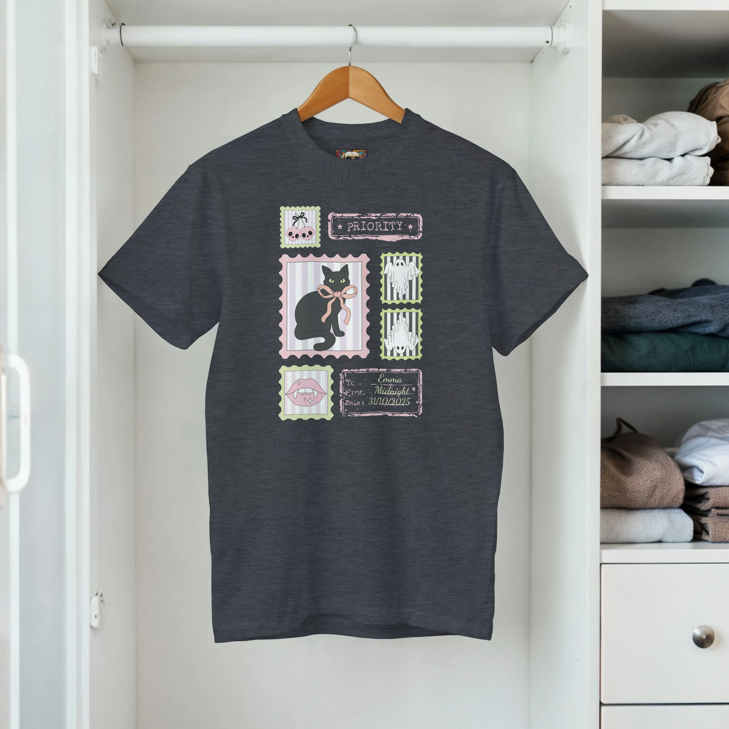 Hanging in a closet a gray t-shirt with a graphic retro stamps Halloween design that includes a black cat and bows.