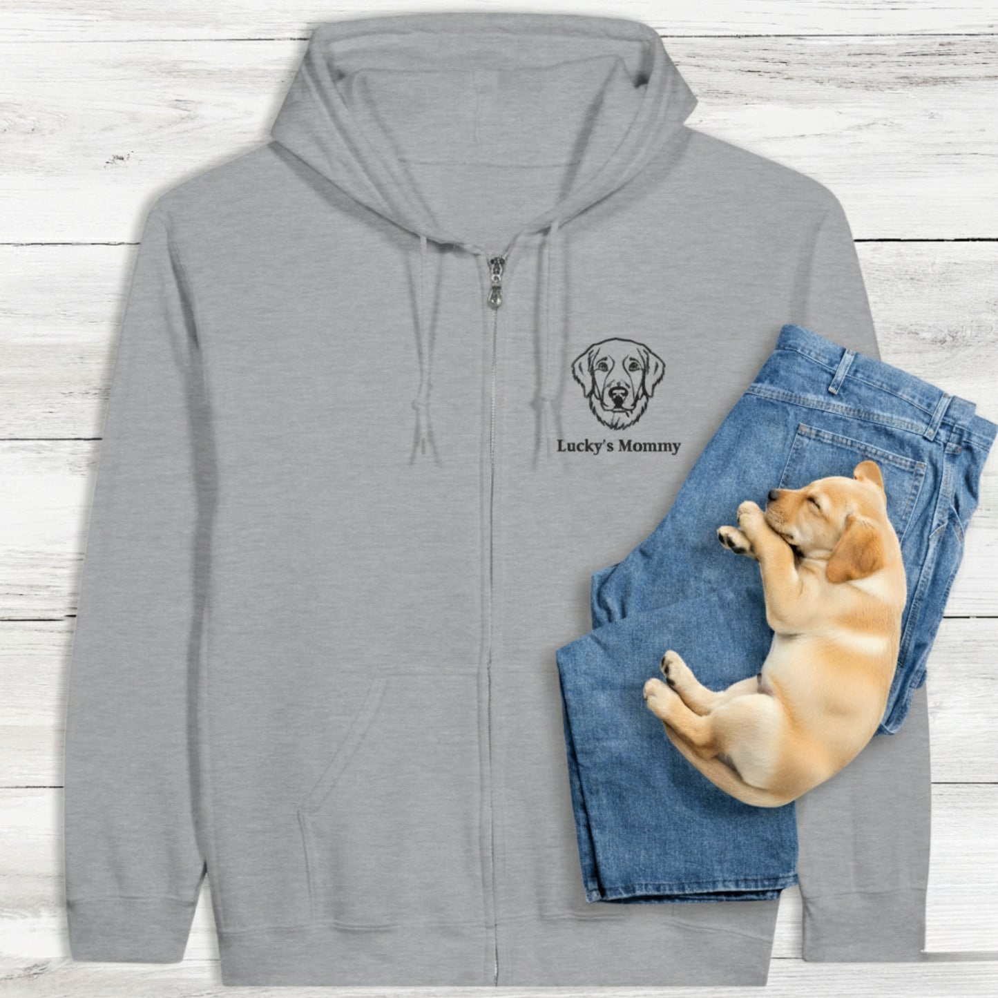 Gray classic zip hoodie with personalised embroidery of dog and text, and a puppy lying on blue jeans. Background is a light wooden surface
