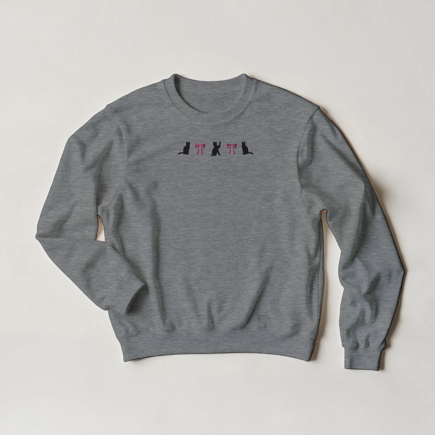 Gray sweatshirt with a embroidery of three black cats and two pink bows. Shirt is flat on a plain background
