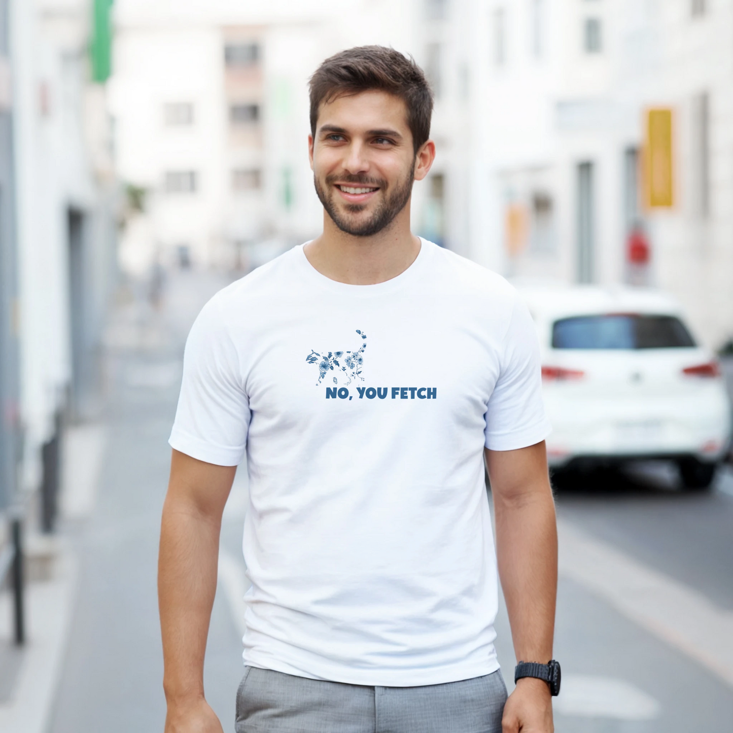 Man wearing a white t-shirt with a cottagecore cat and witty text, 'No,you fetch' while walking down a street.