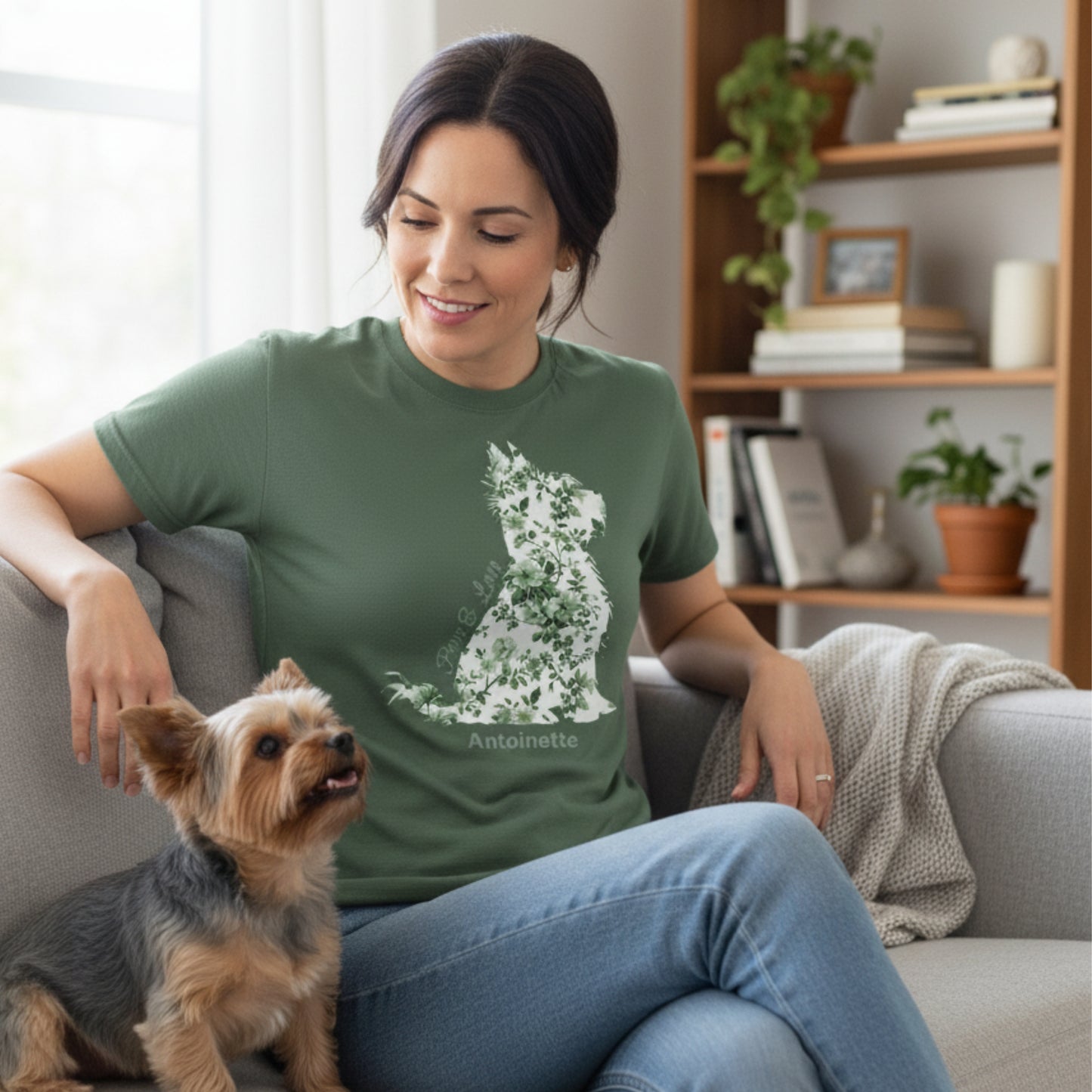 Casually dressed woman seated on sofa wearing military green Gildan 5000 Yorkie Lover Tee with green Toile de Jouy Yorkshire Terrier print; gazing fondly at her Yorkie in cozy living room.