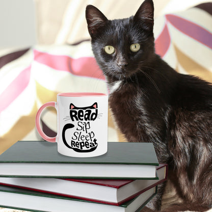 Black cat sitting next to a stack of books.On top of them is a pink color inside mug with 'Read Sip Sleep Repeat' text inside of a black cat with pink ears.