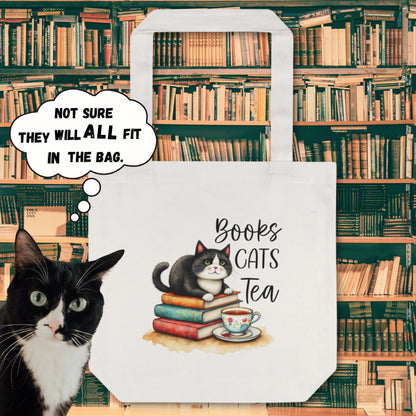 Cotton tote bag with an illustration of a cat sitting on a stack of books with a cup of tea, with a background of a library setting. A cat is looking at the camera with a speech bubble saying 'NOT SURE THEY WILL ALL FIT IN THE BAG'.