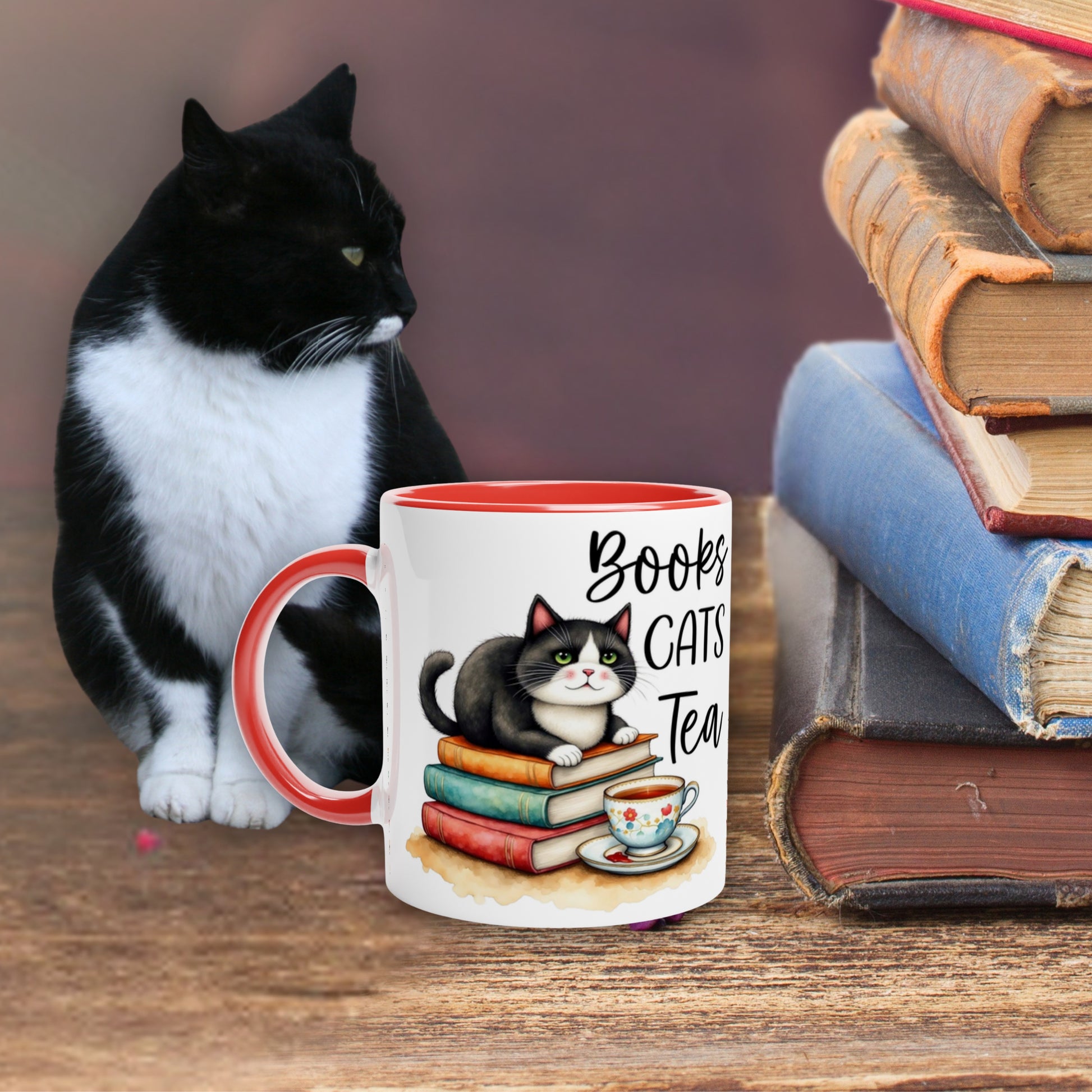 Tuxedo cat sitting next to a mug with a cat illustration and text 'Books Cats Tea' on a wooden table with books.