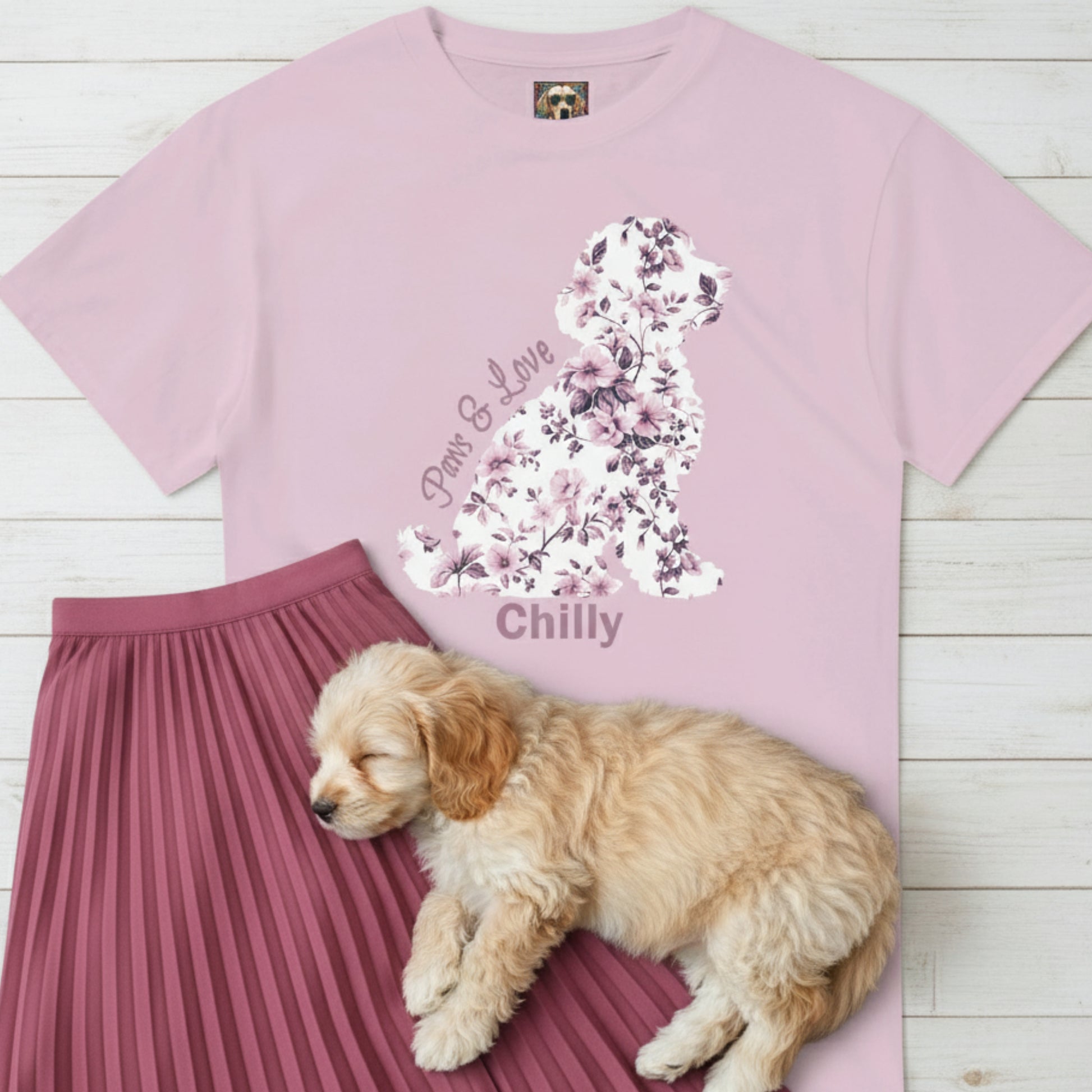 Pink t-shirt with Coquette Toile de Jouy  floral dog design and text, 'Paws & Love' plus the dog's name, pink skirt, and sleeping Cavoodle puppy on a wooden floor.