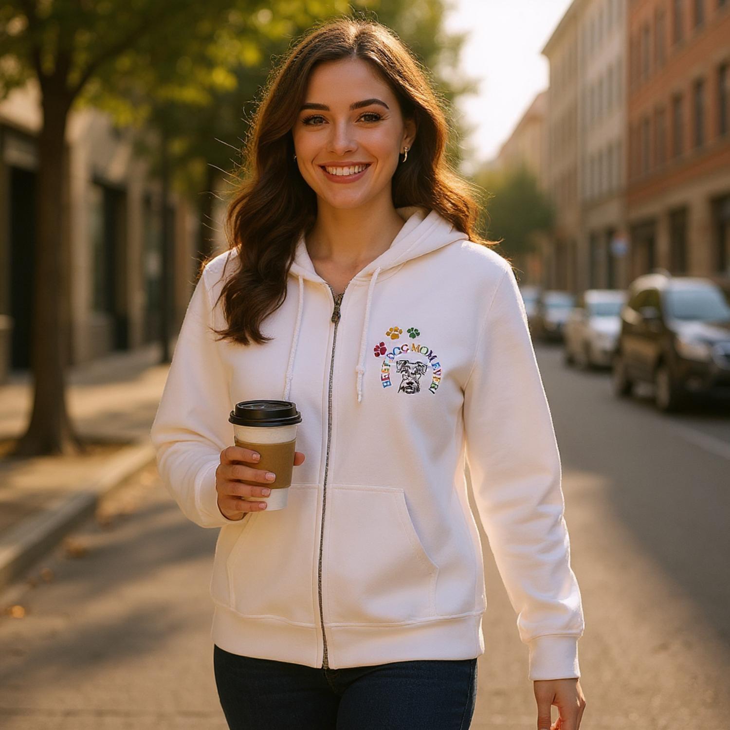 Woman in a white Zipper hoodie with a colorful embroidery design of a dog, dog paws and the words, Best Dog Mom Ever!. The woman is holding a coffee cup while walking on a city street.