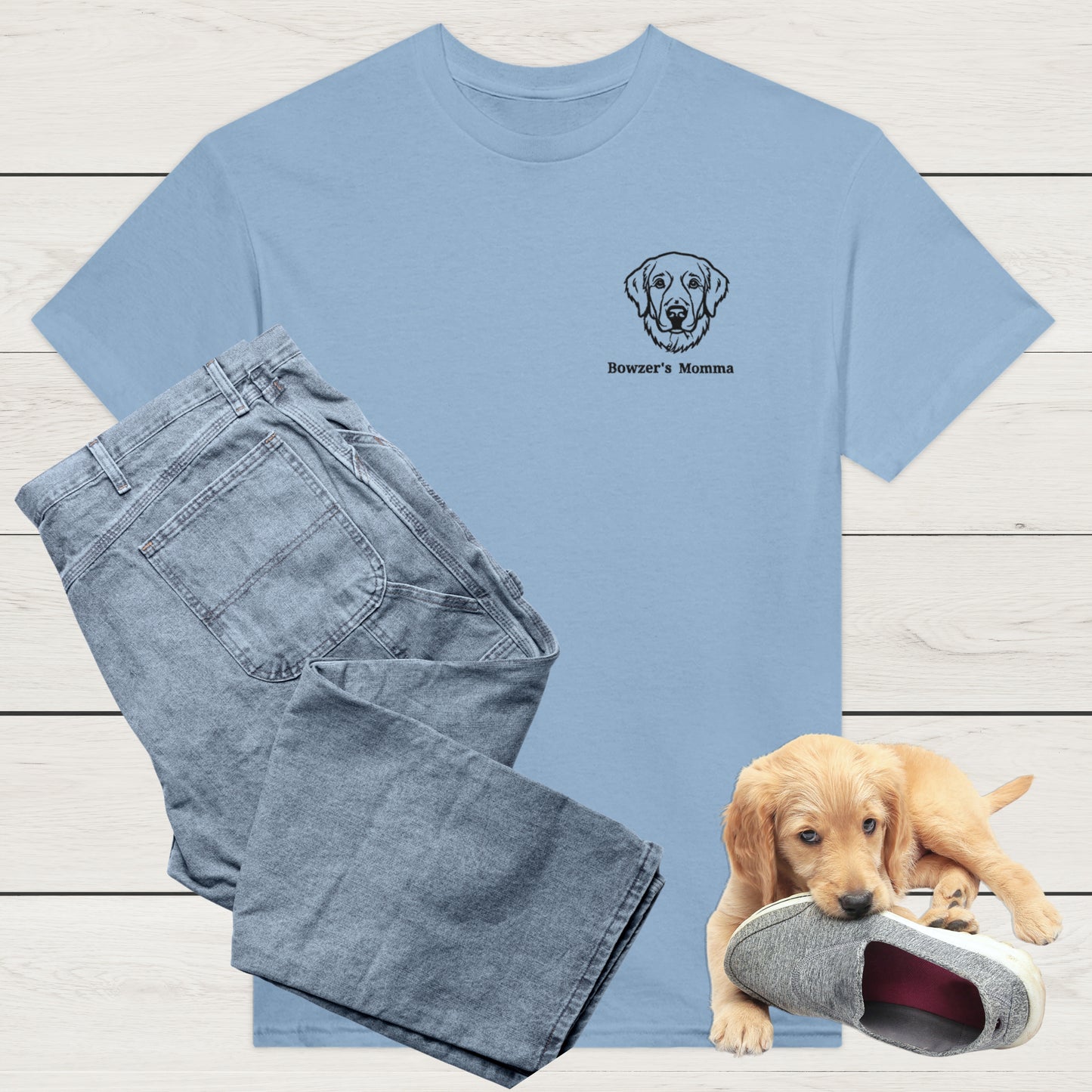 light blue t-shirt with custom embroidery of a dog and personalised text along with wardrobe suggestion of blue jeans on a wooden surface, with a puppy playing with a shoe in the background.