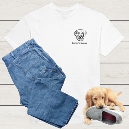 White t-shirt with custom embroidery of a dog and personalised text along with wardrobe suggestion of blue jeans on a wooden surface, with a puppy playing with a shoe in the background.
