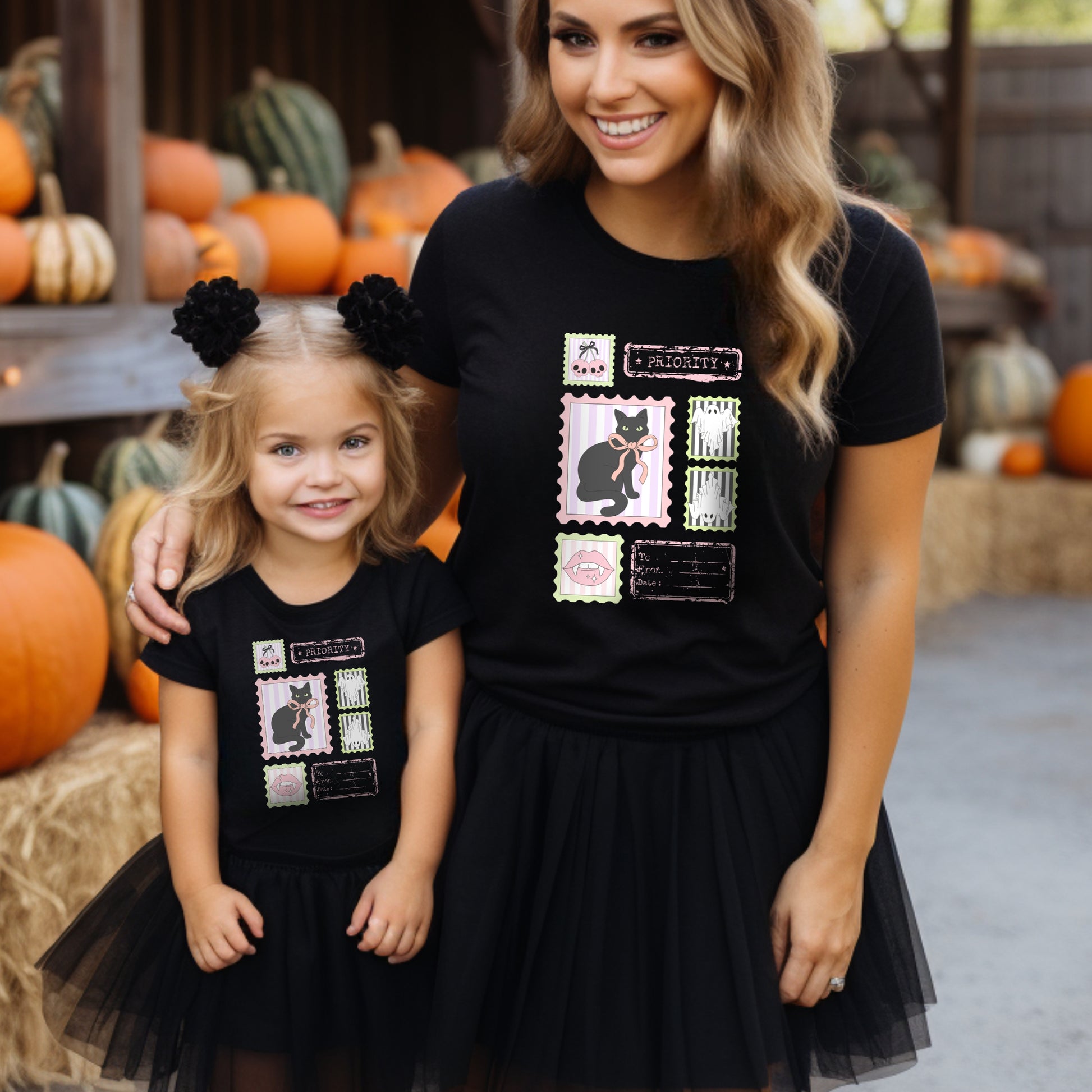 Woman and child wearing black t-shirts with Pink Halloween-themed designs in a pumpkin patch.