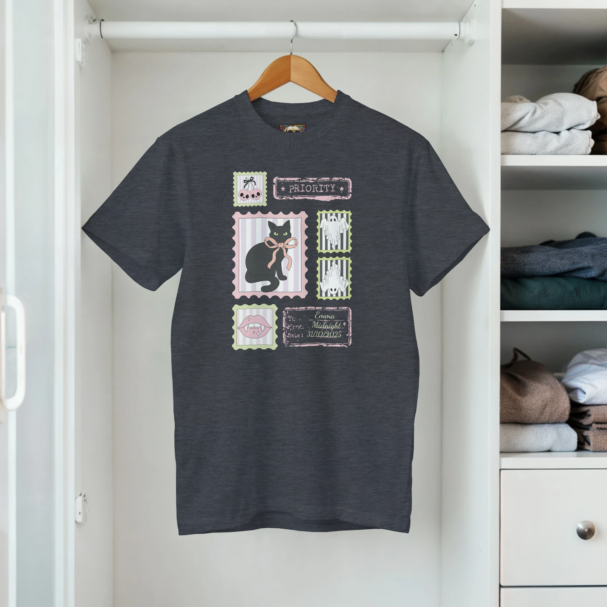 Hanging in a closet a gray t-shirt with a graphic retro stamps Halloween design that includes a black cat and bows.