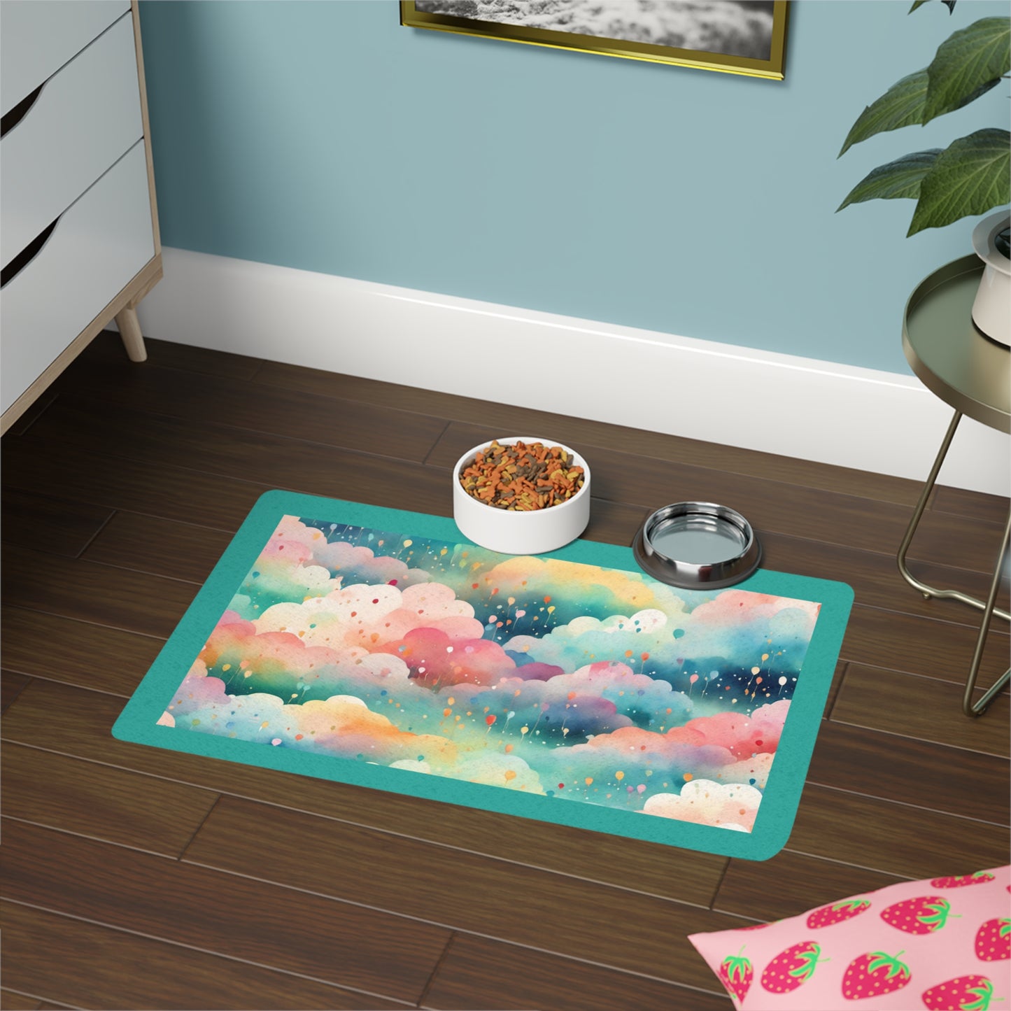 A rectangular pet bowl mat with a dreamy teal background and a playful design of fluffy pastel clouds and balloons. A bowl of pet food is placed on the mat, which is positioned on a hardwood floor next to a plant.
