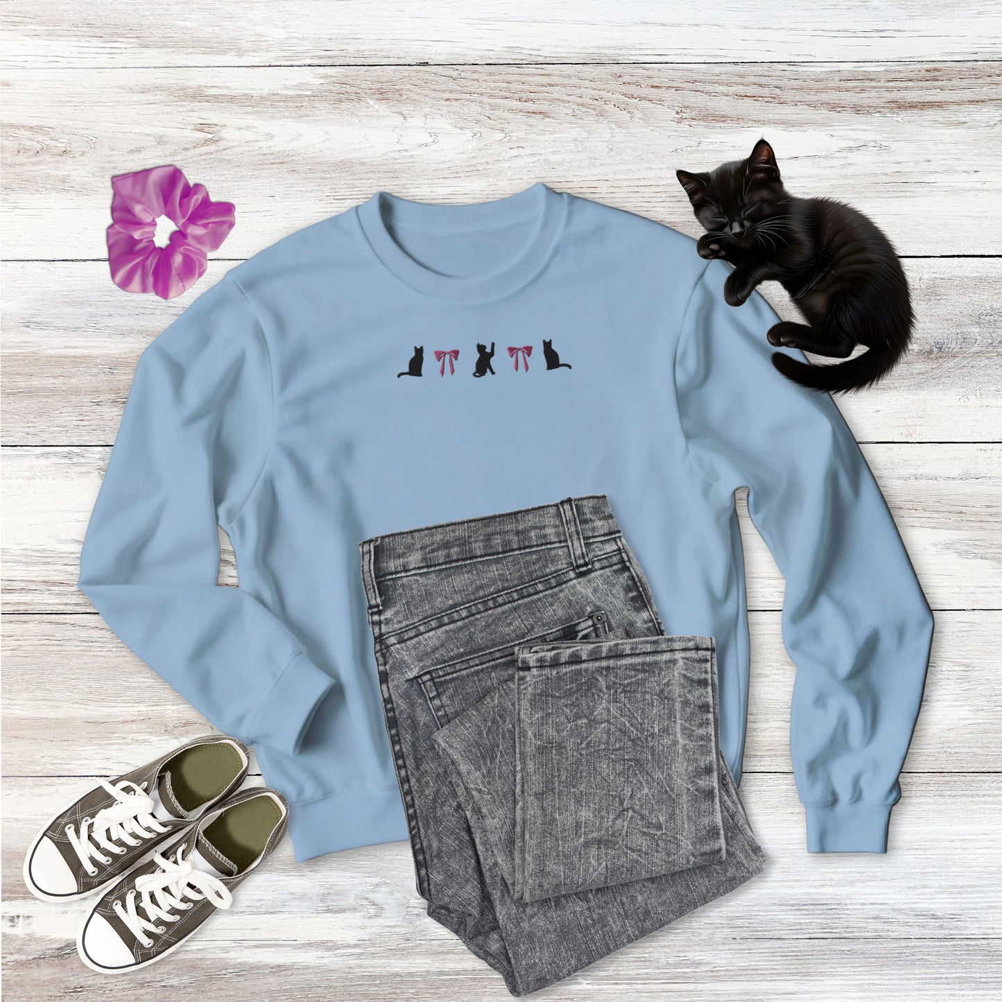 Embroidered Coquette Pink Bows and Black Cats  Gildan Sweatshirt in light blue on wooden background with outfit style suggestion and sweet black kitten sleeping.