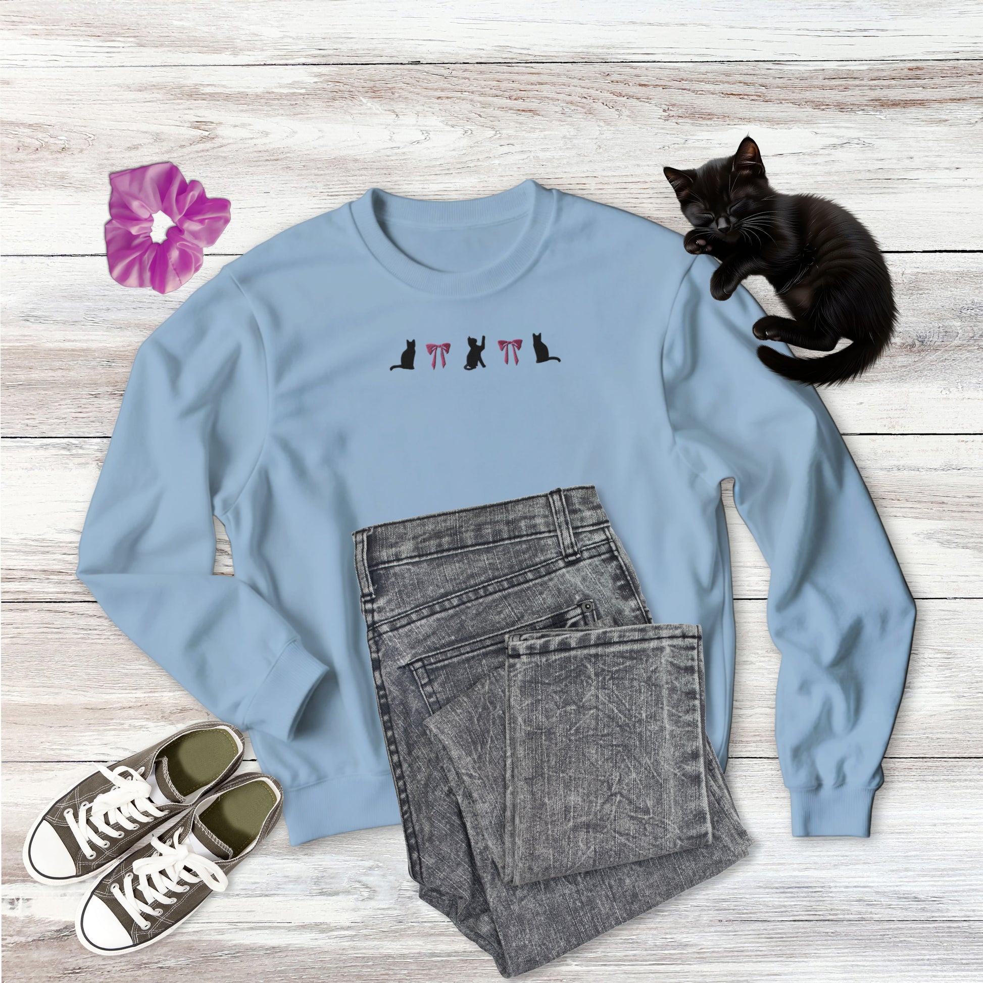Embroidered Coquette Pink Bows and Black Cats  Gildan Sweatshirt in light blue on wooden background with outfit style suggestion and sweet black kitten sleeping.