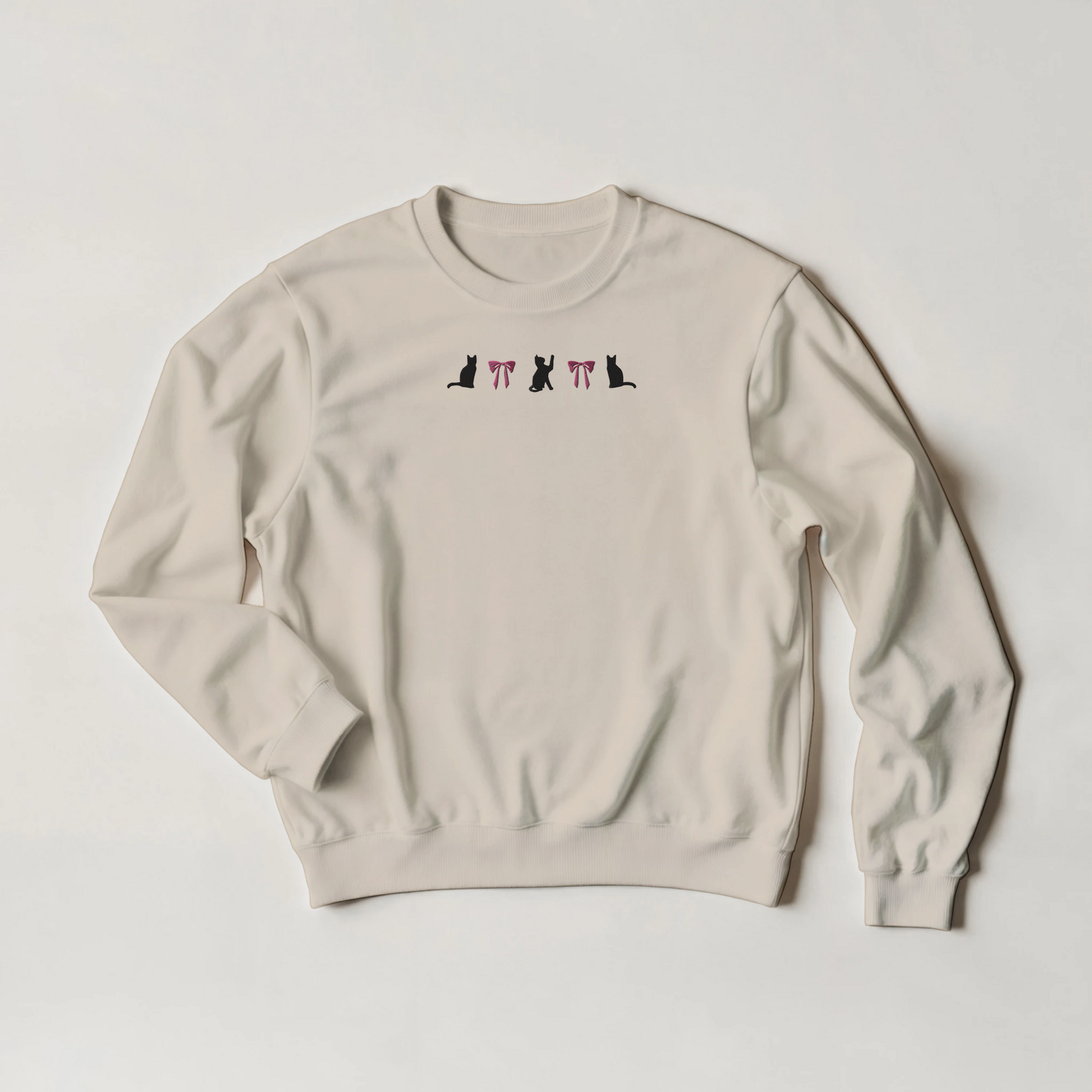 SAnd beige sweatshirt with black cats and pink bows embroidery across the front. The shirt is flat on a plain background.