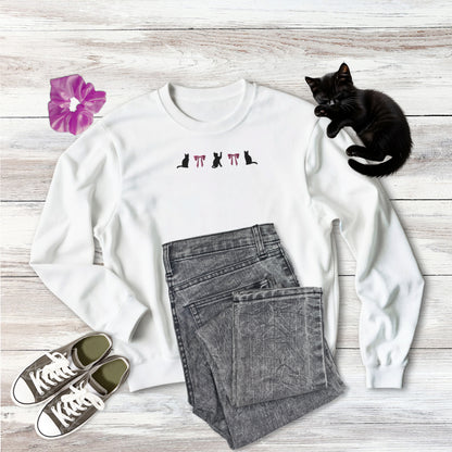 Embroidered Coquette Pink Bows and three Black Cats Halloween Gildan Sweatshirt in white on wooden background with outfit style suggestion and sweet black kitten sleeping.