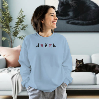 Woman wearing a light blue sweatshirt with emboridered black cat and pink coquette bow design in a living room with a black cat lounging on a modern sofa.