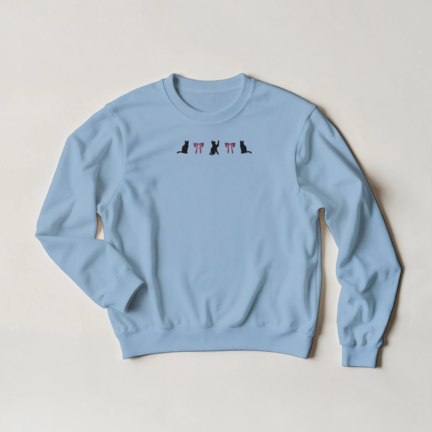 Light blue sweatshirt with black cats and pink coquestte bows emboidery  on a plain background