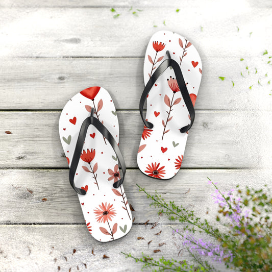 Flip Flops, Pink Floral print with hearts are light weight sandles in picture these women's slip-on shoes are on a light wooden deck sprinkled with beach sand and flowers. 