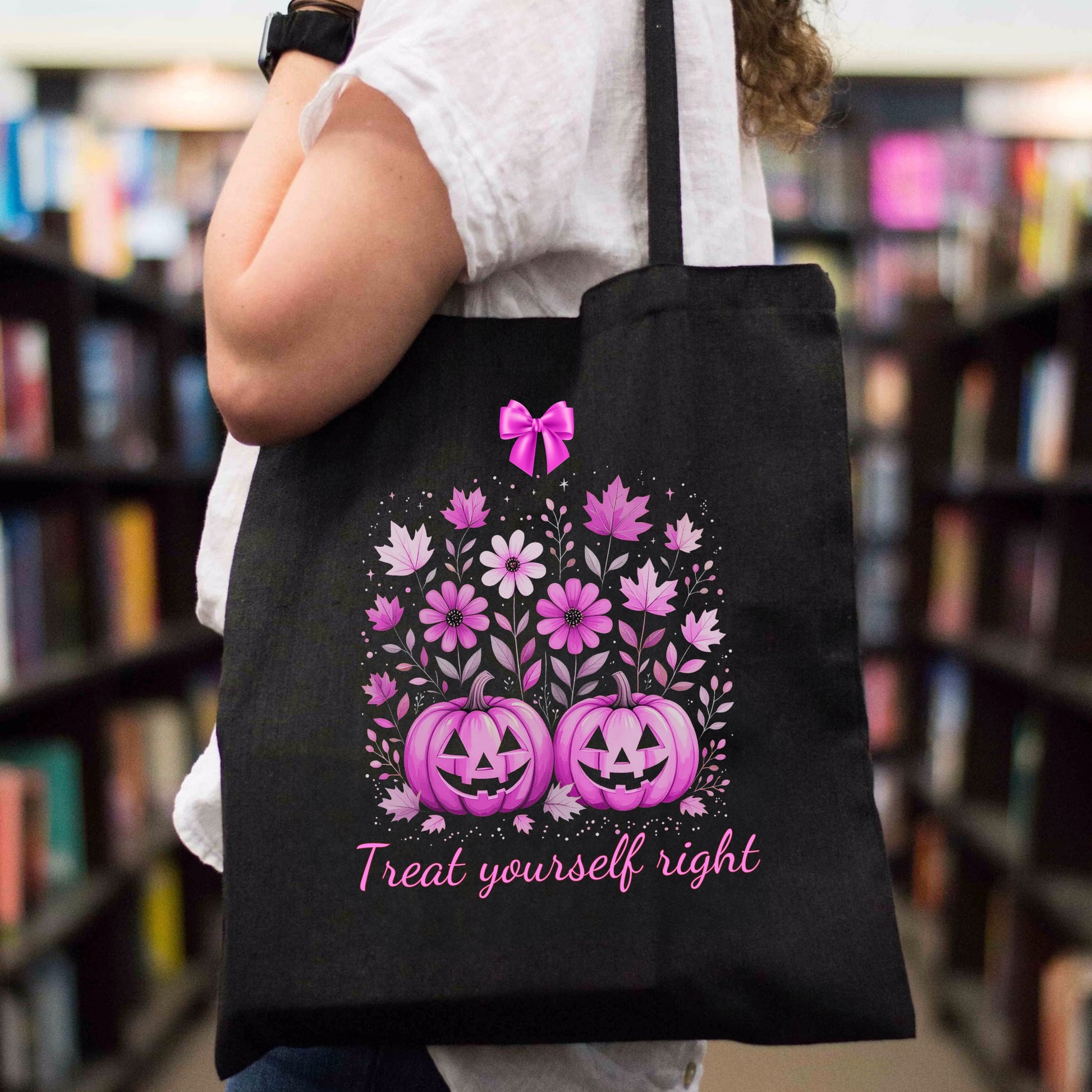Black tote bag with pink Halloween spooky floral and pumpkin design held by a person in a bookstore.