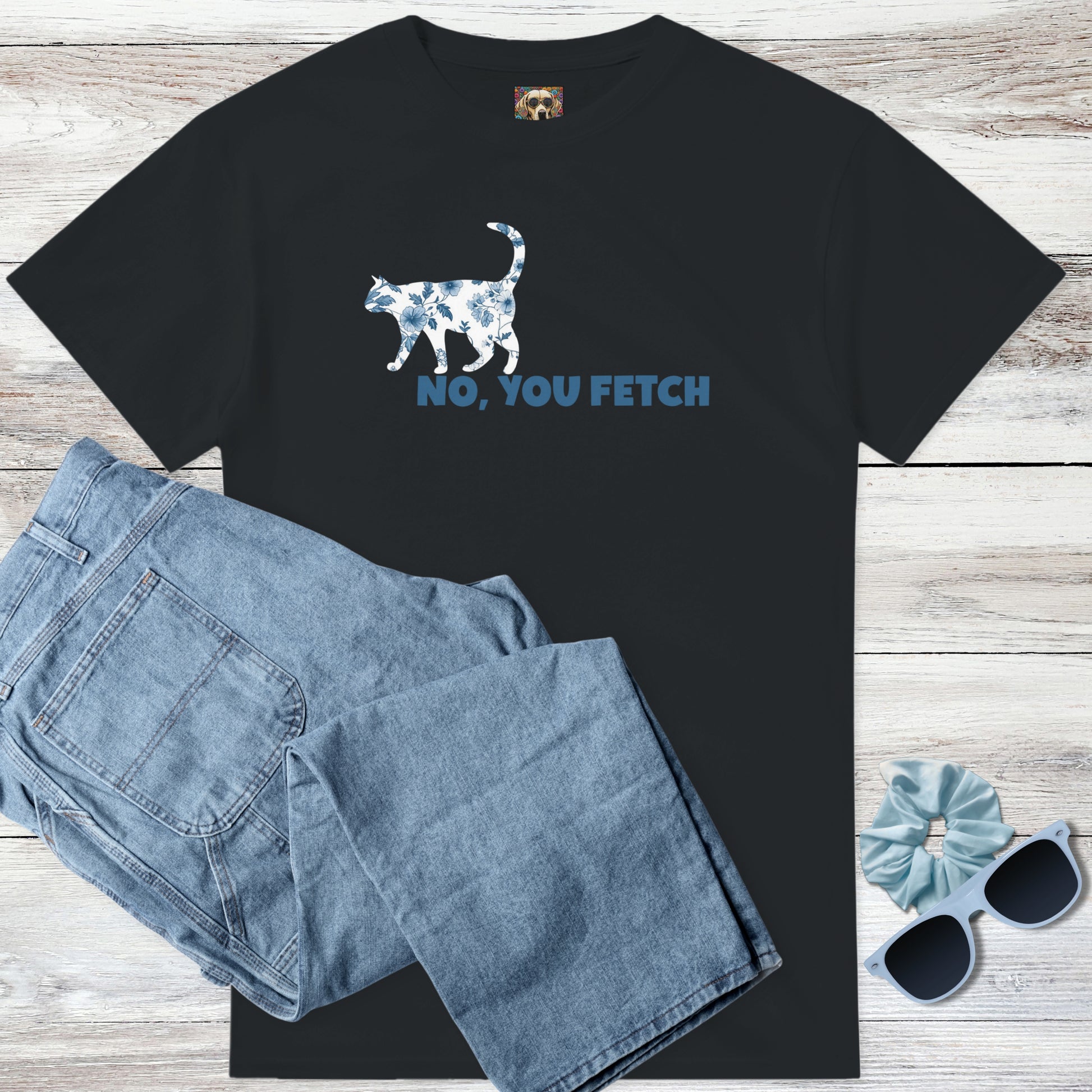 Black toile de jouy cottagecore blue and white flowers on a cat t-shirt with witty 'NO, YOU FETCH' text, and outfit suggestion - blue jeans, sunglasses, and scrunchie on a wooden surface.