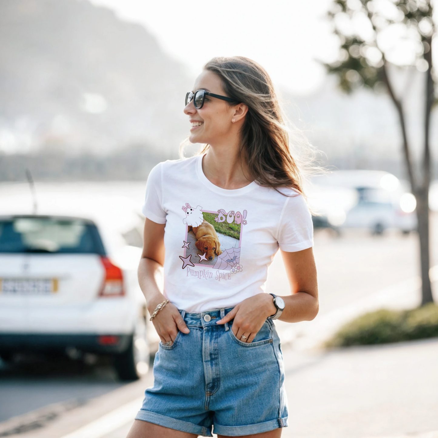 Woman wearing a white t-shirt with a Coquette pink Halloween picture frame graphic design standing outdoors