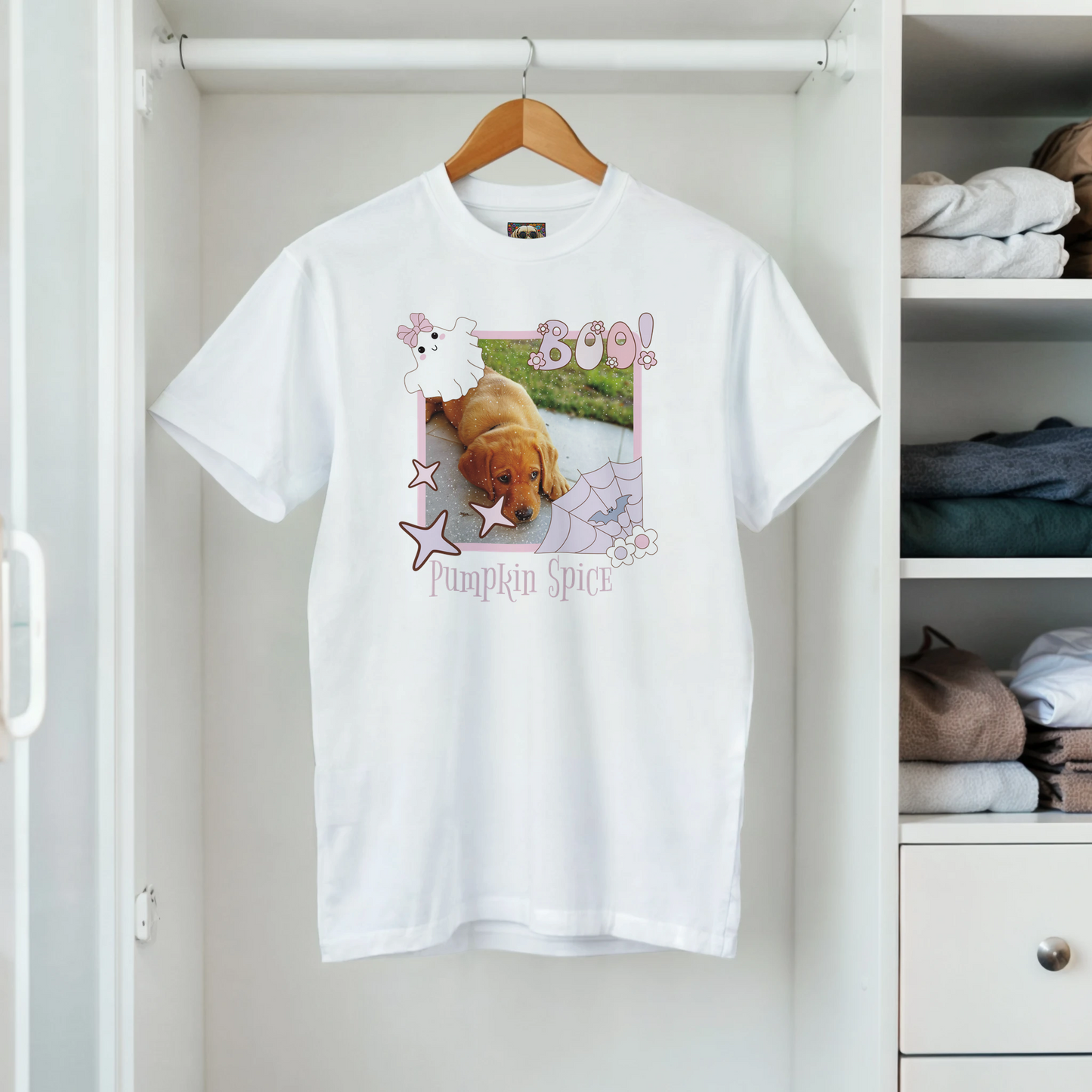 White t-shirt with a Coquette Pink Halloween picture frame graphic with a photo of a cute puppy inside it. Below is the  name, 'Pumpkin Spice in spooky font. The soft cotton tee is on a hanger in a closet.