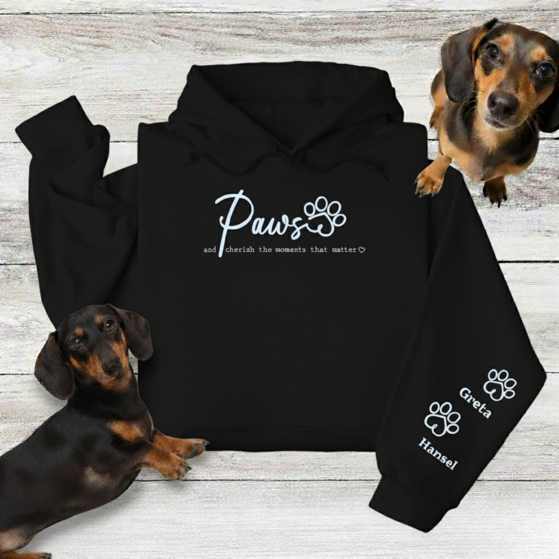 Personalise an embroidered black hooded sweatshirt with up to four pets' names shown with 2 Dachshunds on a wooden surface.