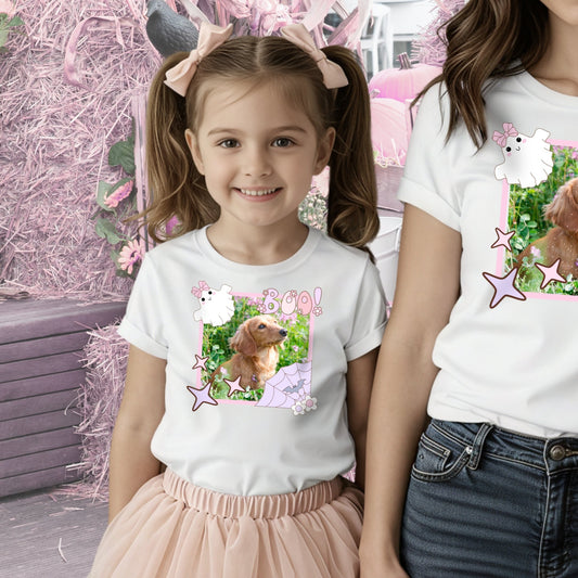 Young girl wearing a t-shirt with a Coquette pink Halloween picture frame graphic that has a picture of a Dachshund inside in a whimsical pink pumpkin patch setting. Her Mother is just out of the frame of the picture.