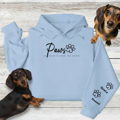 Light blue Gildan Hooded Sweatshirt with Custom Embroidery - up to 4 names on sleeves. Embroidery on the front of this shirt reads, 'Paws and cherish the moments that matter.' Flatlay with 2 Dachshunds