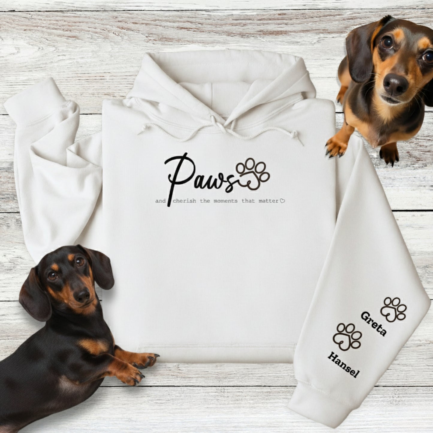 White Gildan Hooded Sweatshirt with Custom Embroidery - up to 4 names on sleeves. Embroidery on the front of this shirt reads, 'Paws and cherish the moments that matter.' Flatlay with 2 Dachshunds