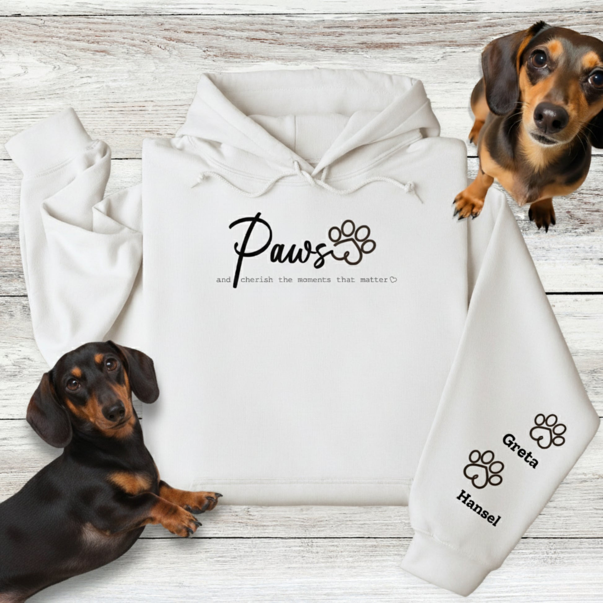 White Gildan Hooded Sweatshirt with Custom Embroidery - up to 4 names on sleeves. Embroidery on the front of this shirt reads, 'Paws and cherish the moments that matter.' Flatlay with 2 Dachshunds