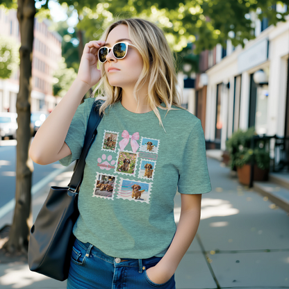Woman wearing a heather mint green t-shirt with colorful graphic designs of her dogs as postage stamps and a pink coquette bow. She is standing in on the sidewalk of a tree lined street.