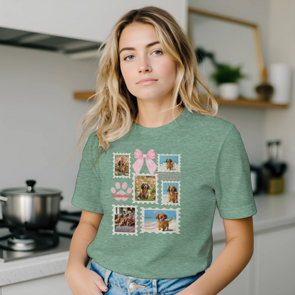 Woman wearing a heather mint green t-shirt with colorful graphic designs of her dogs as postage stamps and a pink coquette bow. She is standing in her kitchen.