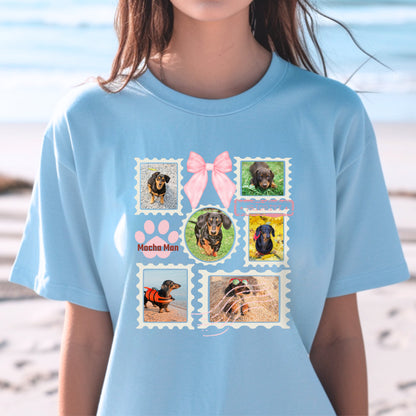 Woman wearing a light blue t-shirt with colorful graphic designs of her dogs as postage stamps and a pink coquette bow. She is at the beach.