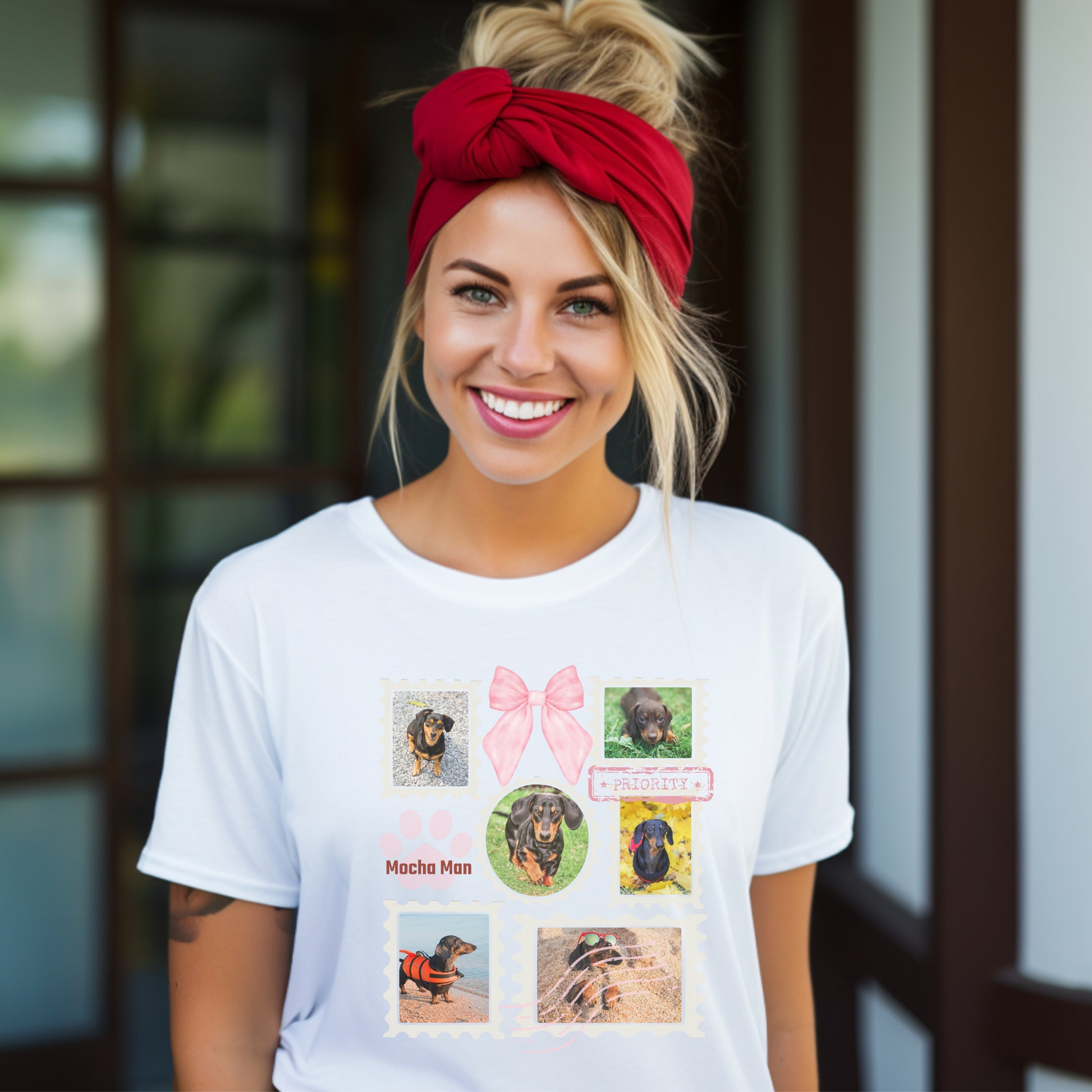 Woman wearing a white t-shirt with colorful graphic designs of her dogs as postage stamps and a pink coquette bow. She has her hair up with a red tie, blurred background of building.