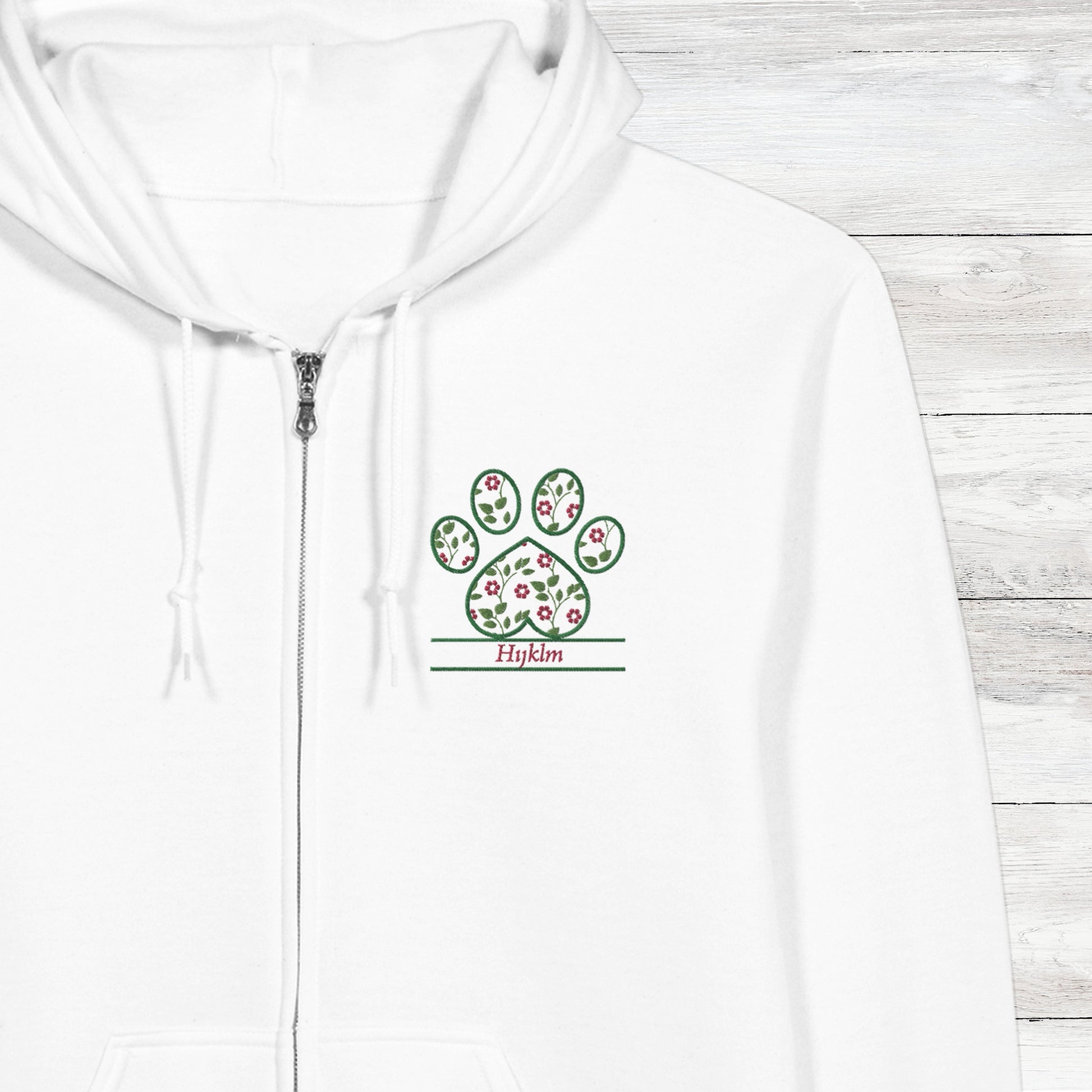 White hoodie with a embroidery floral paw print design close up with pet's name option on a wooden surface