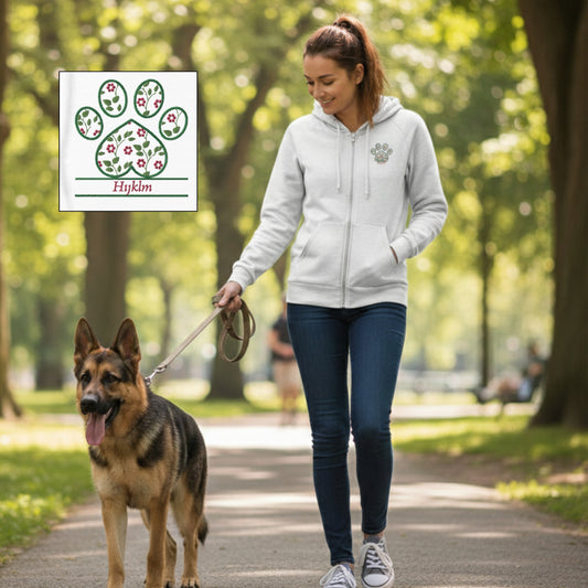 Woman wearing an eco-friendly white zip front hoodie with a cottagecore pink floral embroidery design on left side. She is walking her German Shepard in a park area. 