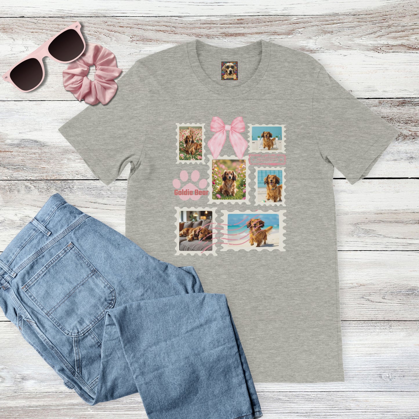 Personalized pet photo gray t-shirt with  design of a postage stamp collage and pink bow next to jeans, pink sunglasses, and hair scrunchie on a wooden surface