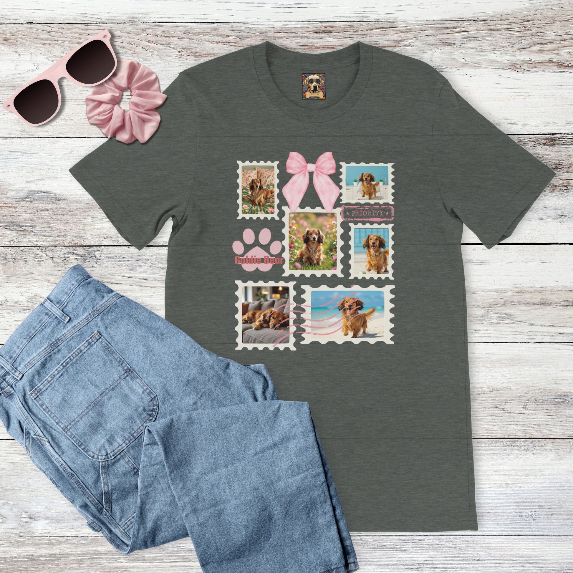 Personalized pet photo dark gray t-shirt with  design of a postage stamp collage and pink bow next to jeans, pink sunglasses, and hair scrunchie on a wooden surface