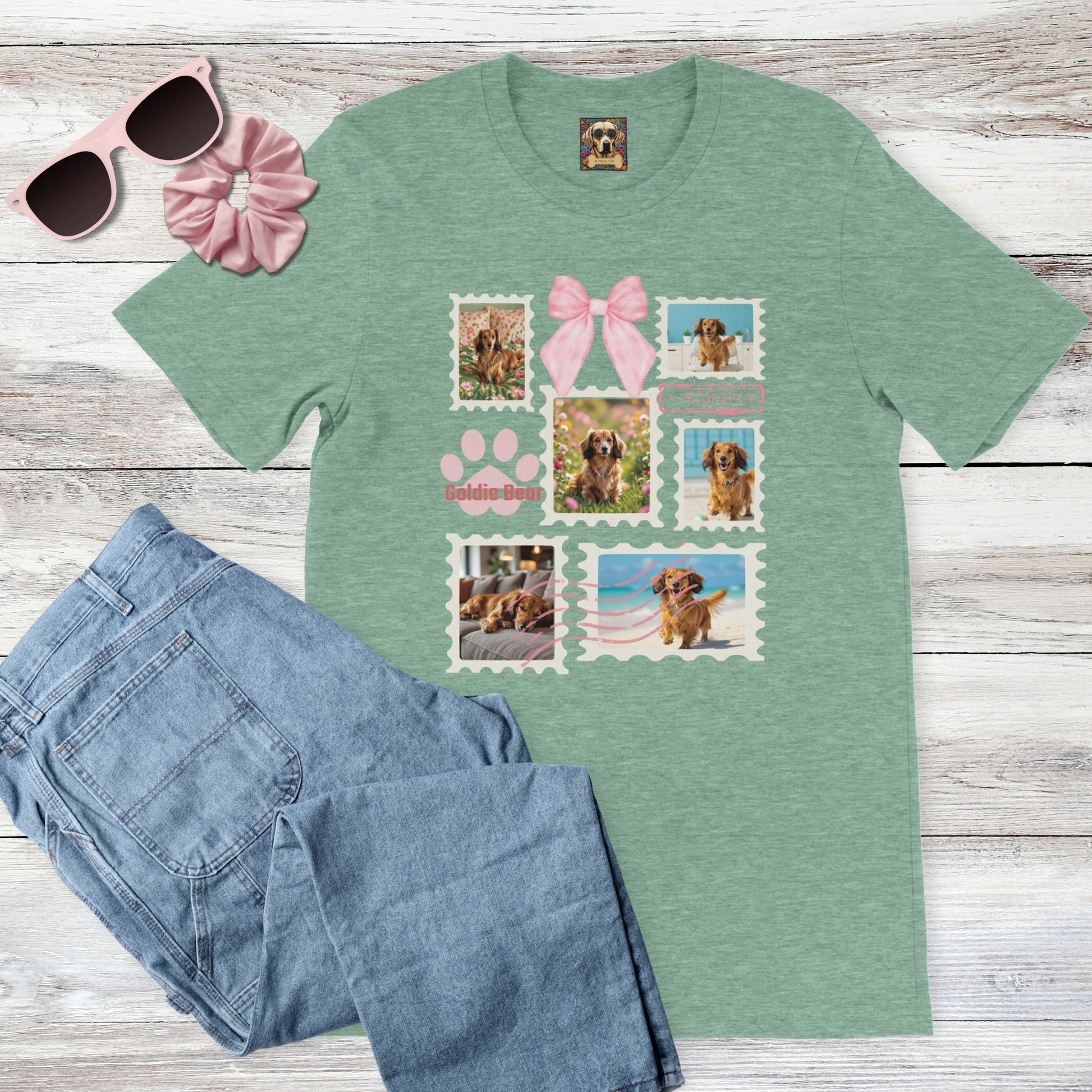 Personalized pet photo heather mint green t-shirt with  design of a postage stamp collage and pink bow next to jeans, pink sunglasses, and hair scrunchie on a wooden surface