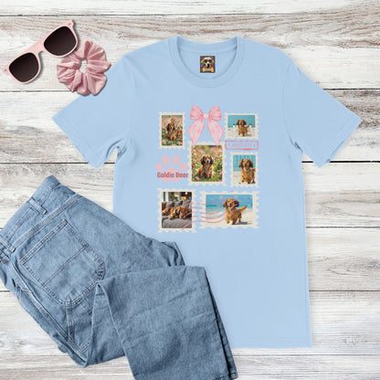 Personalized pet photo light blue t-shirt with  design of a postage stamp collage and pink bow next to jeans, pink sunglasses, and hair scrunchie on a wooden surface