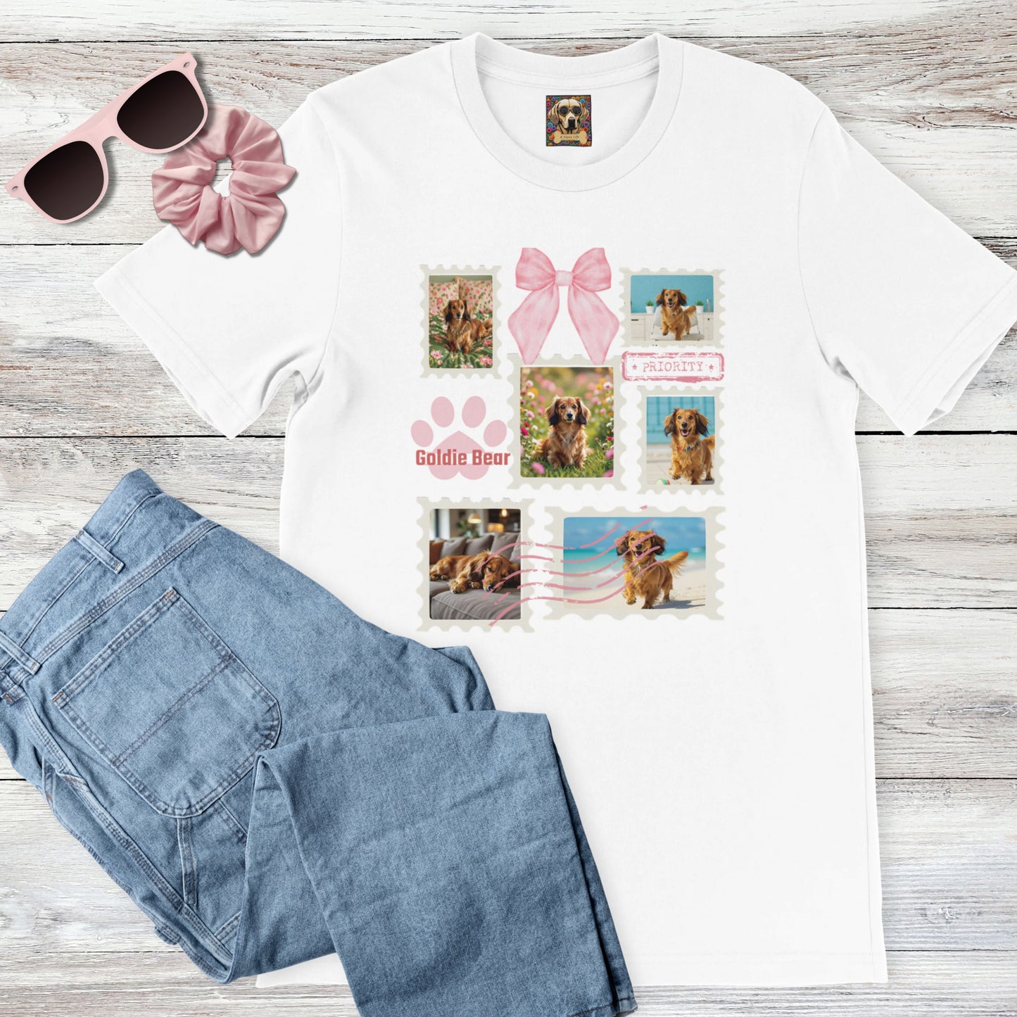 Personalized pet photo white t-shirt with  design of a postage stamp collage and pink bow next to jeans, pink sunglasses, and hair scrunchie on a wooden surface