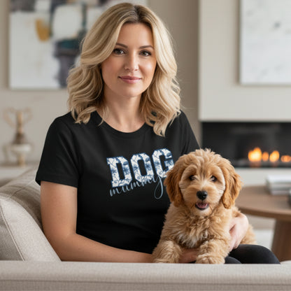 Woman wearing a black t-shirt with 'DOG mom' text, holding a small brown dog in a living room.