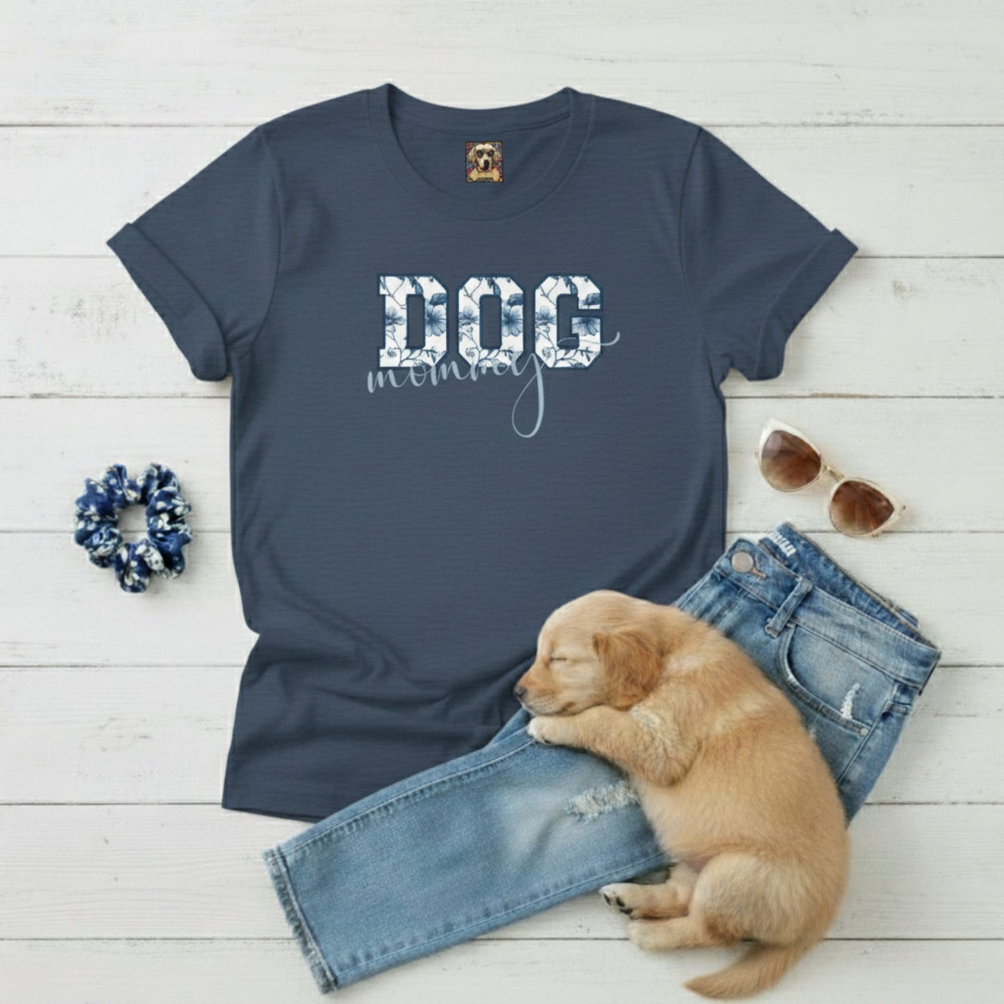 Navy blue t-shirt with 'DOG mom' text, puppy, jeans, scrunchie, and sunglasses on a light wooden surface