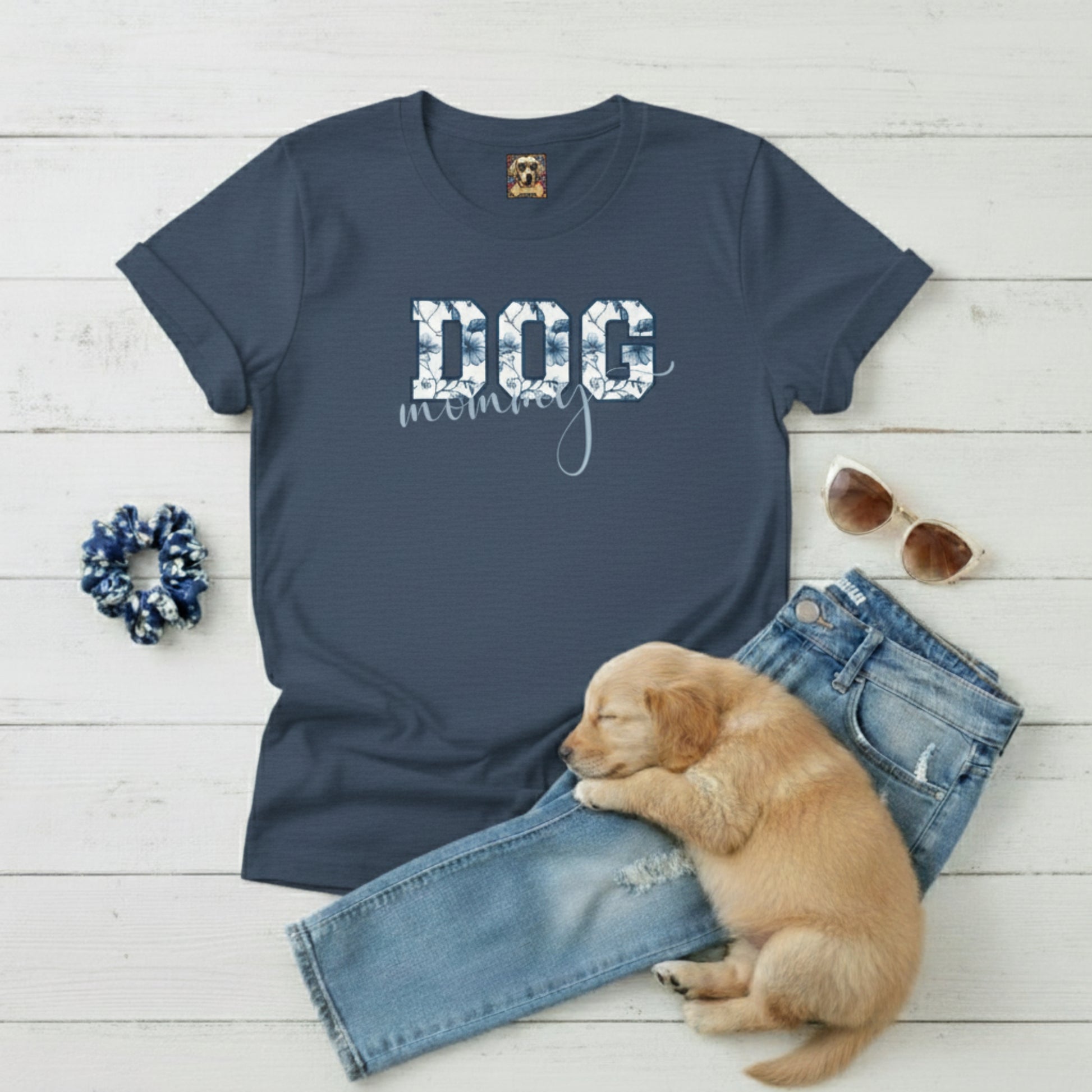 Navy blue t-shirt with 'DOG mom' text, puppy, jeans, scrunchie, and sunglasses on a light wooden surface