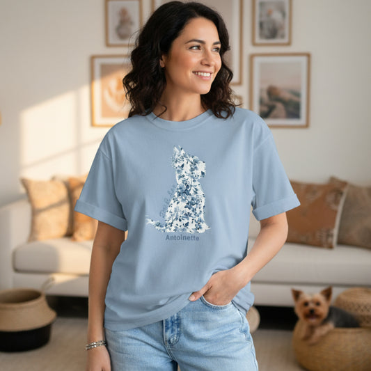 Woman in faded jeans wearing oversized Gildan 5000 light blue Yorkie Lover Tee with blue Toile de Jouy Yorkshire Terrier print; casual chic look in boho living room with Yorkie puppy in basket.
